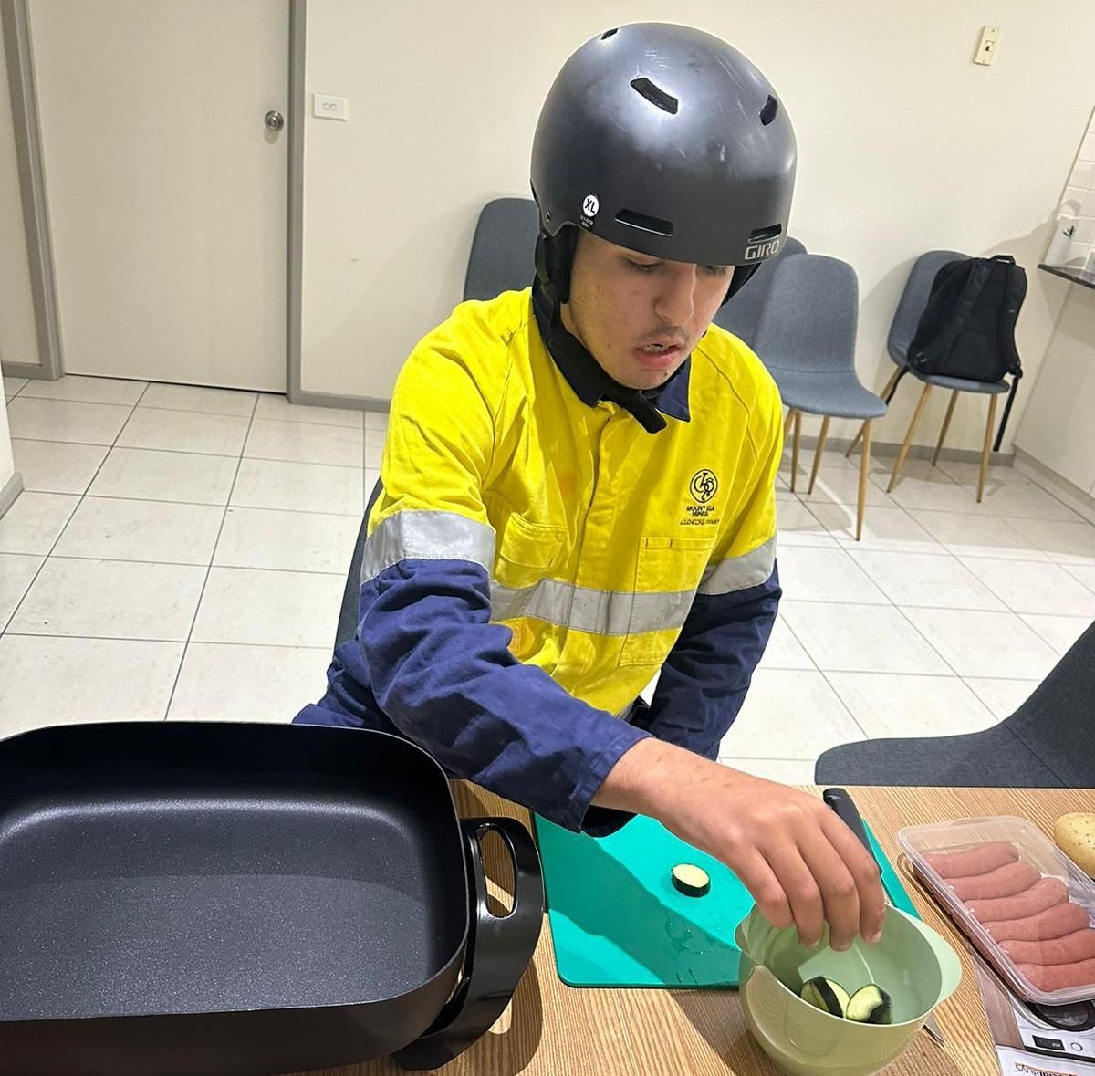 A man wearing a helmet and a yellow shirt is preparing food. SIL – Supported Independent Living, NDIS, Canberra