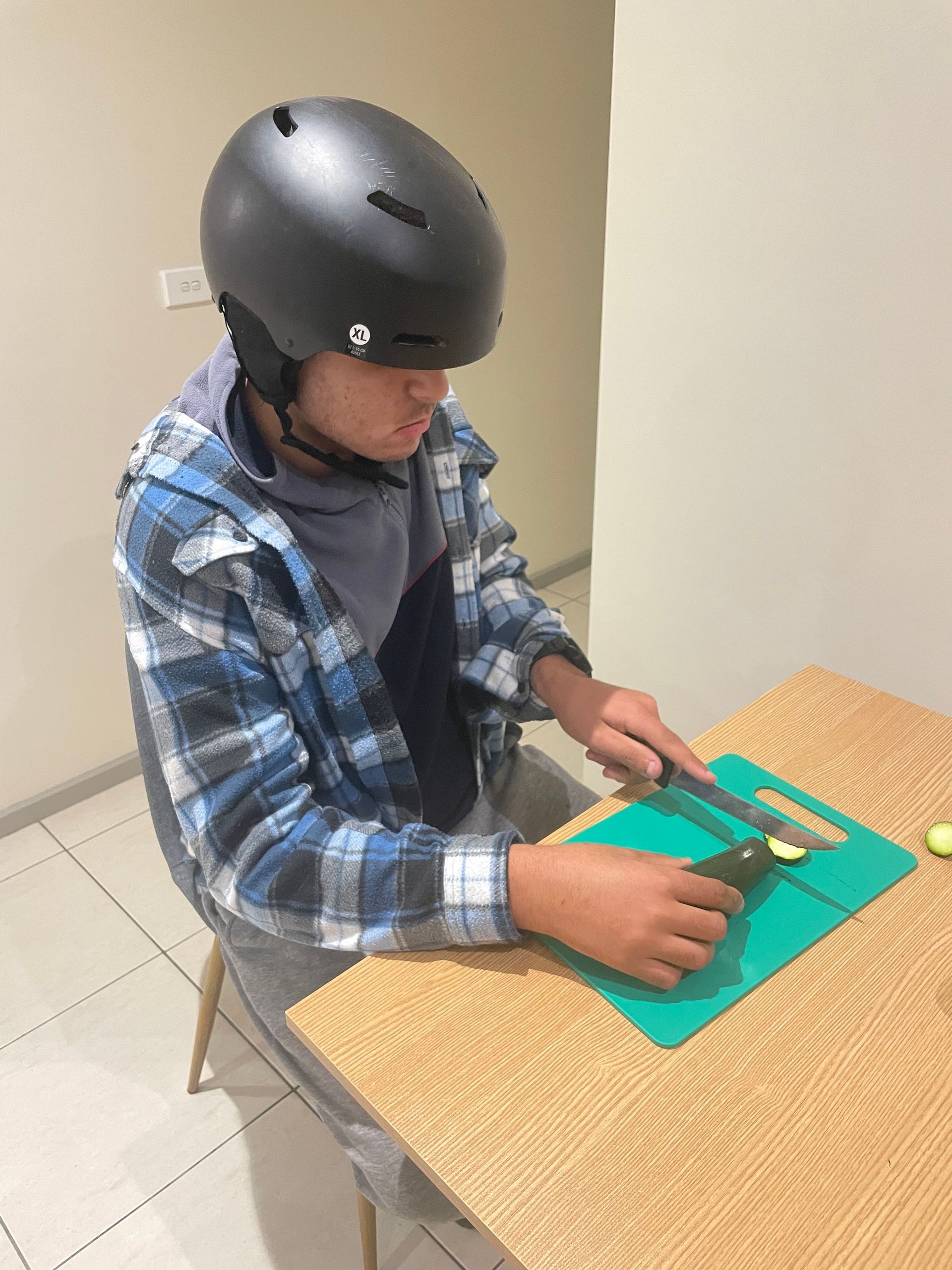 A young boy wearing a helmet is cutting vegetables on a cutting board.