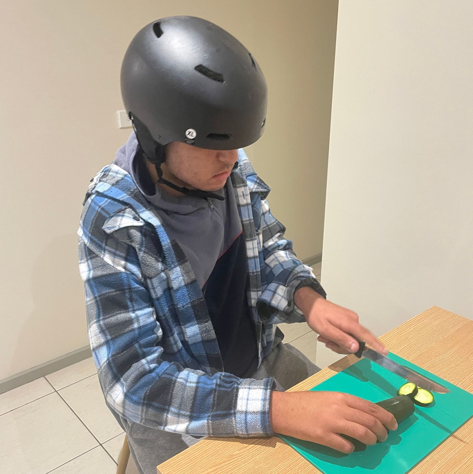 A young boy wearing a helmet is cutting vegetables on a cutting board. NDIS support in Gungahlin and Canberra-Wide