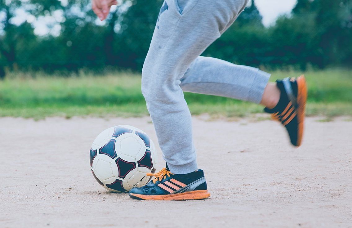 A person is kicking a soccer ball on a dirt field.