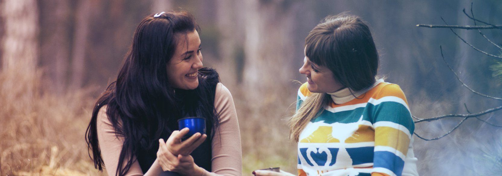 Two women are sitting around a campfire in the woods. SIL – Supported Independent Living, NDIS, Canberra