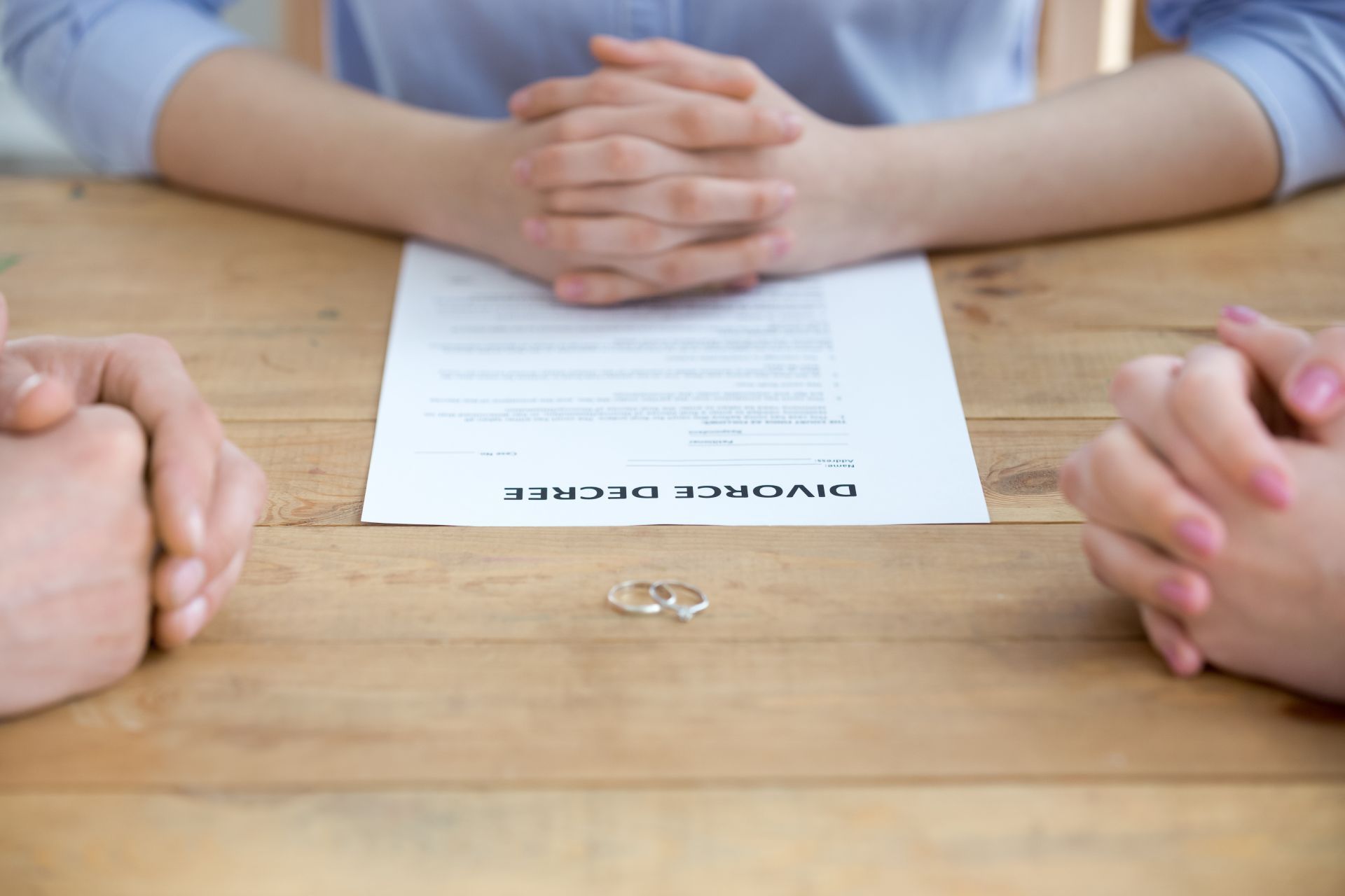 Divorce decree on a table with hands and rings, symbolizing separation.