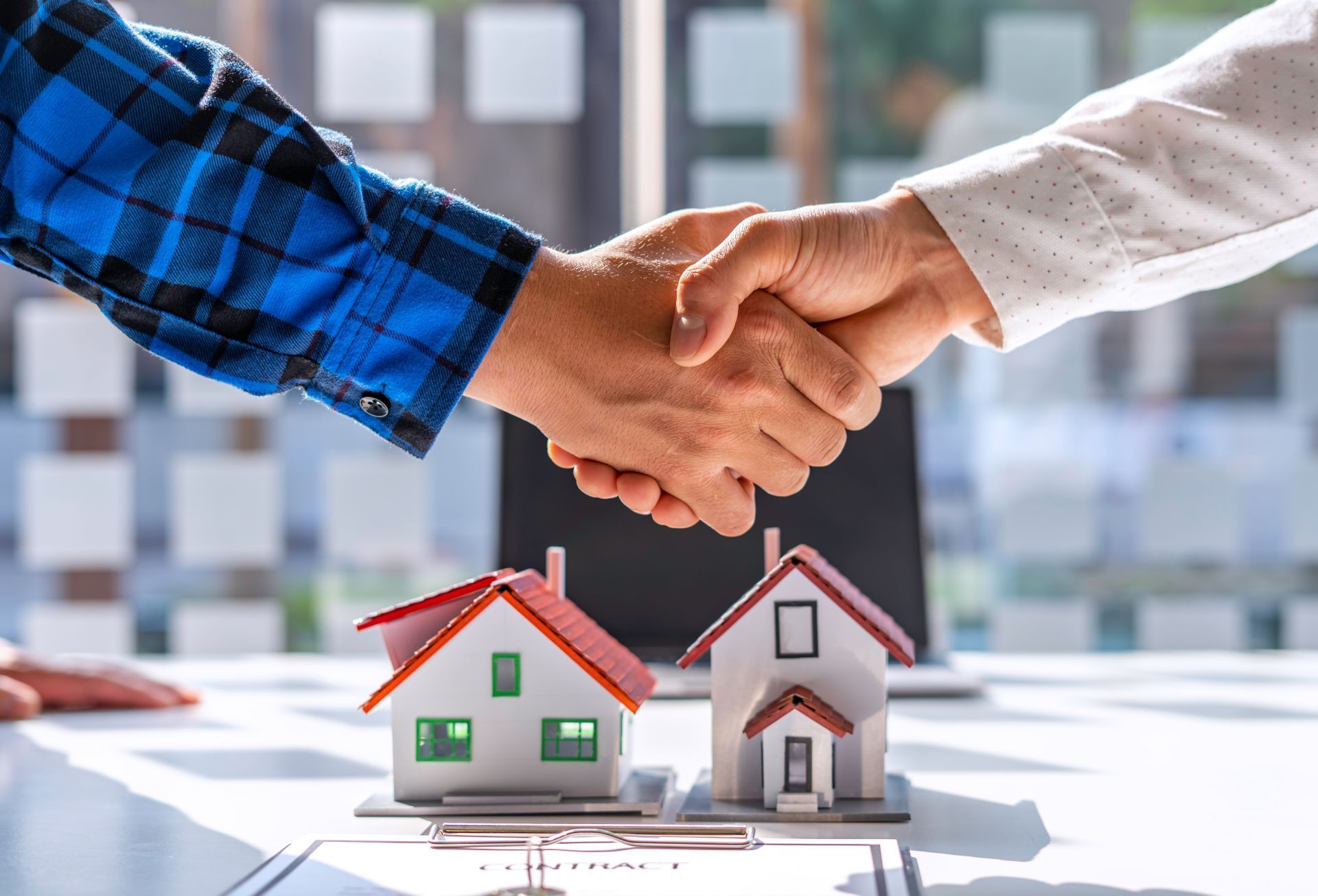 Two people shaking hands over miniature house models and a contract.