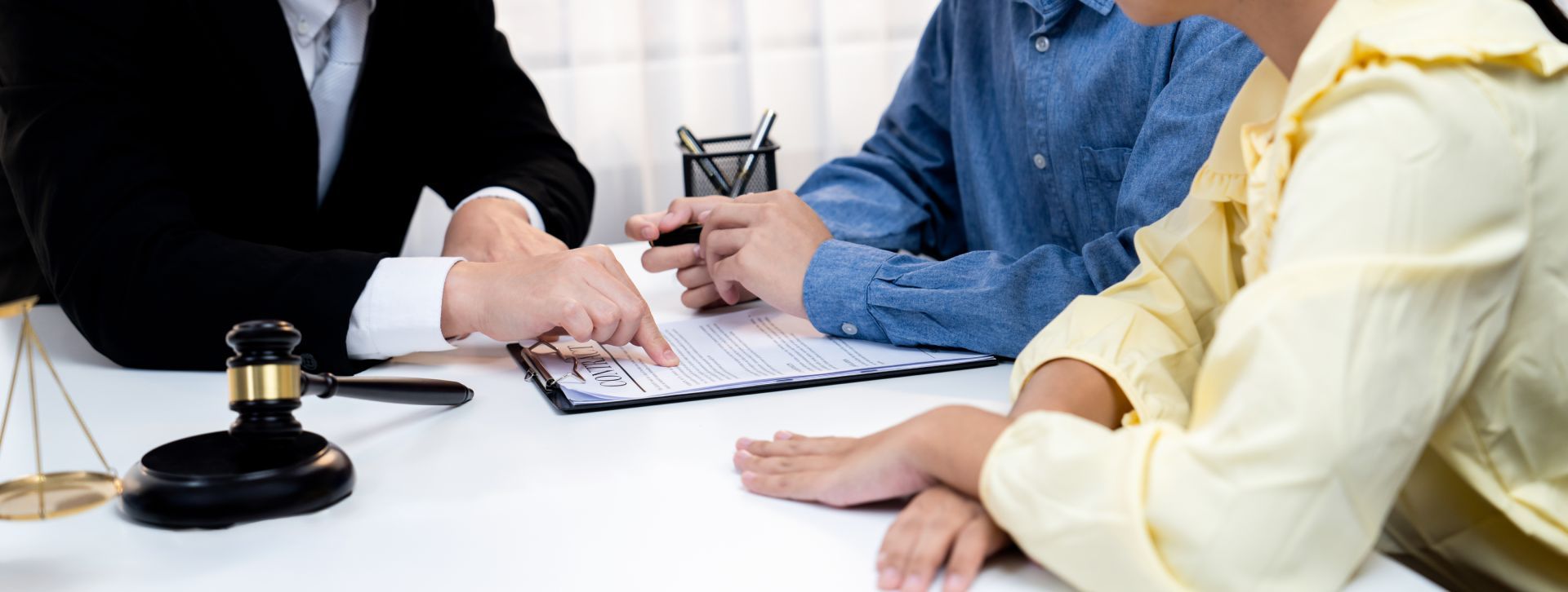 People meeting with a lawyer to review documents. A gavel and scales of justice are in the foreground.