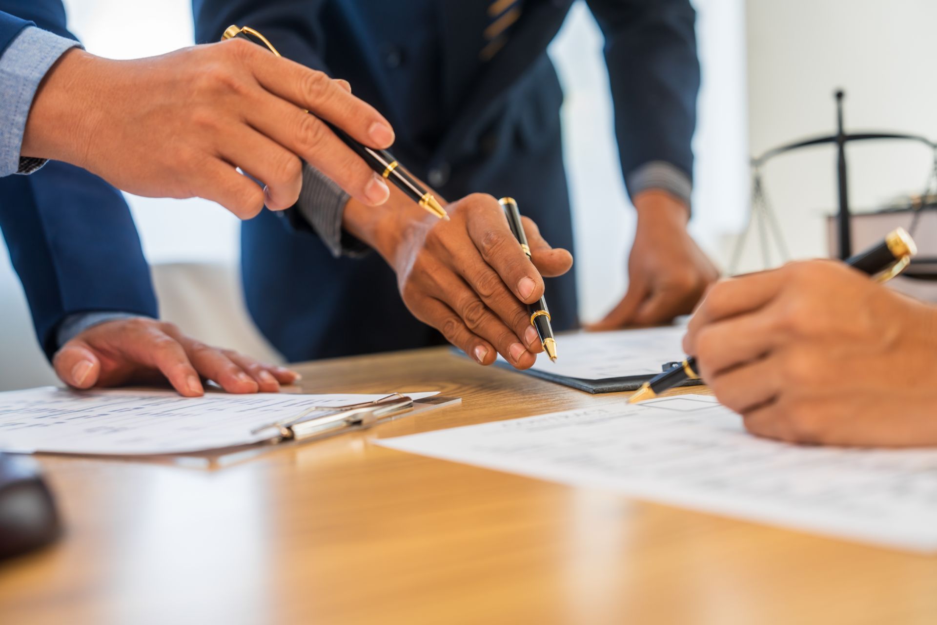 People in suits examining documents and pointing with pens at a table.