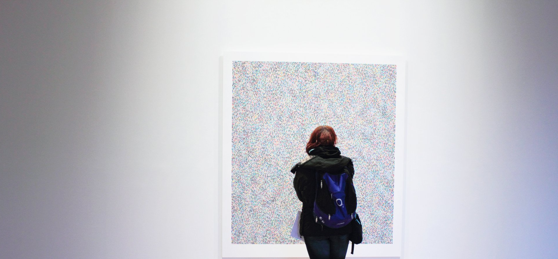 A woman with a backpack is looking at a painting on a wall.