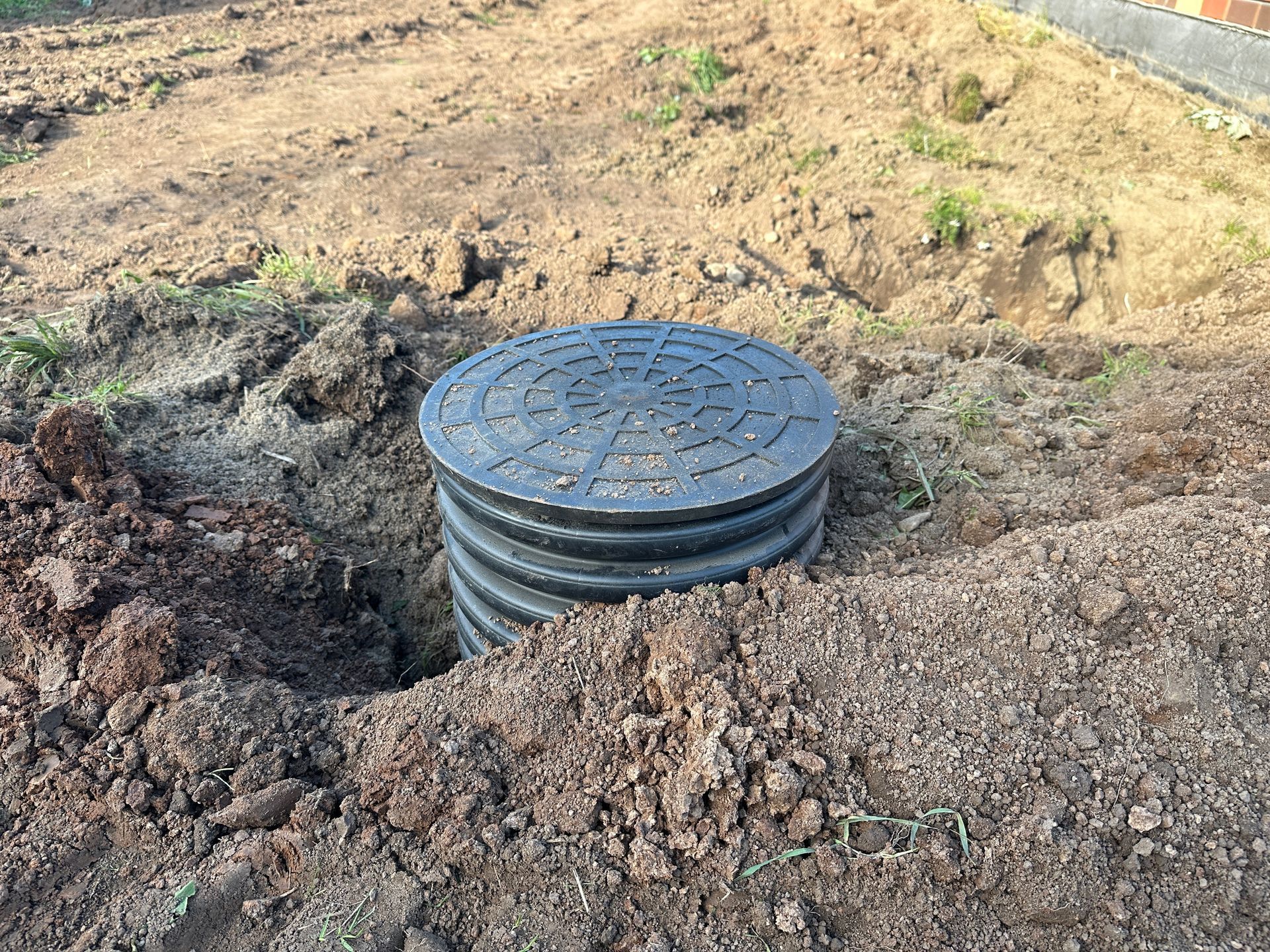 An outdoor irrigation pump system with green doors, pipes, and a filter tank, partially recessed in a grassy yard.