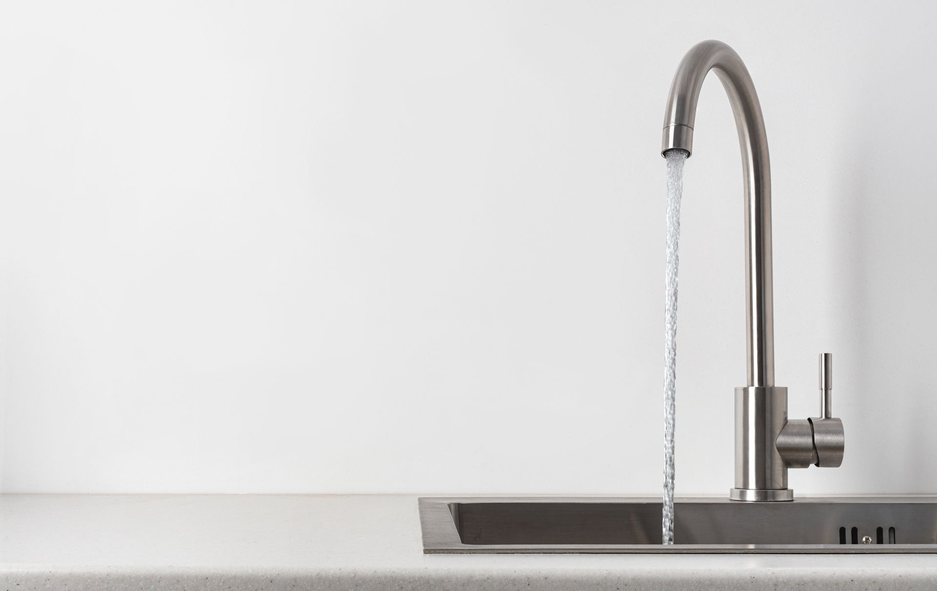 Stainless steel faucet with running water over a sink, against a white background.