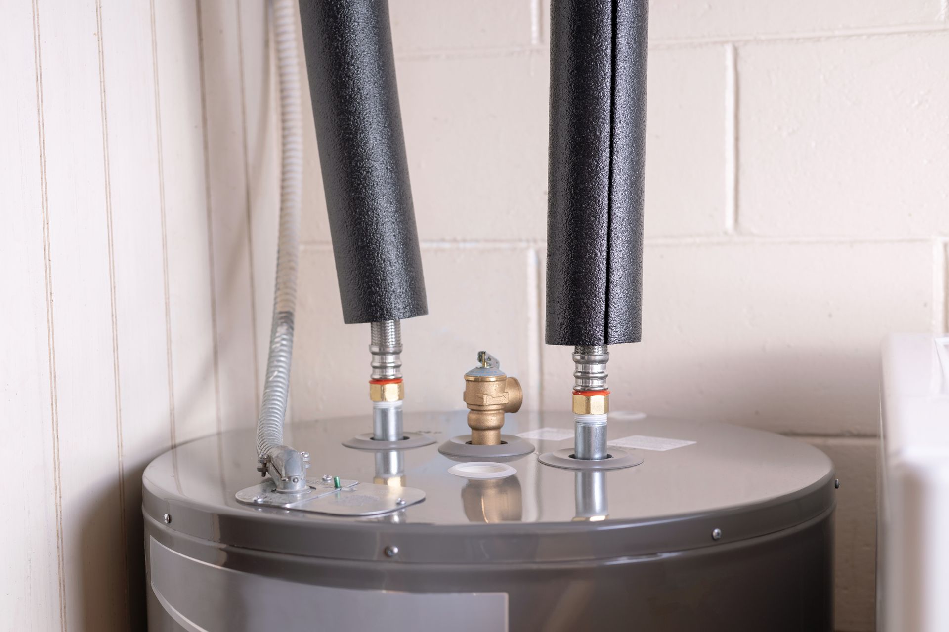 Water heater with insulated pipes against a white brick wall.