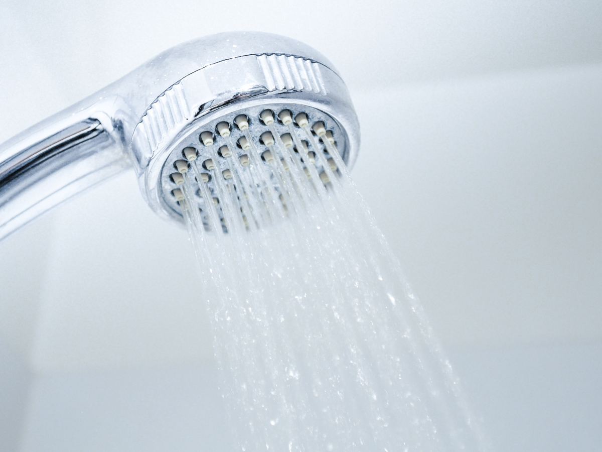 Chrome shower head spraying water against a white background.