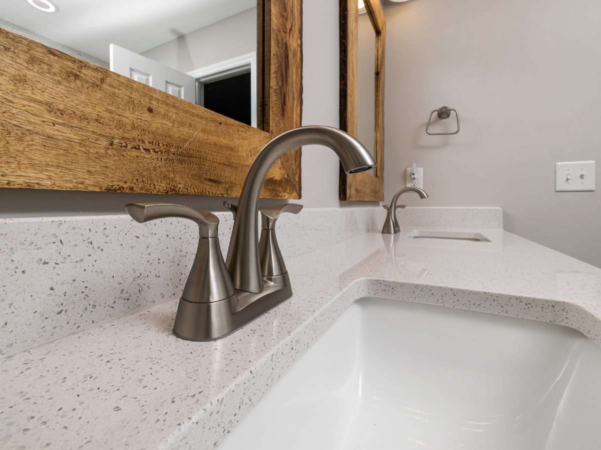 Bathroom sink with brushed nickel faucet, light speckled countertop, and wooden mirror frame.