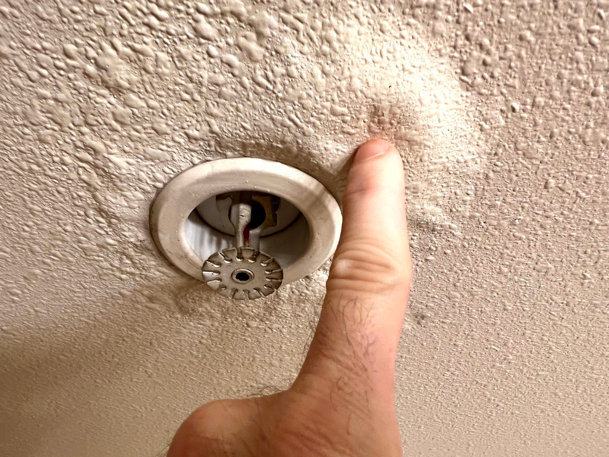 A person is pointing at a fire sprinkler on the ceiling.