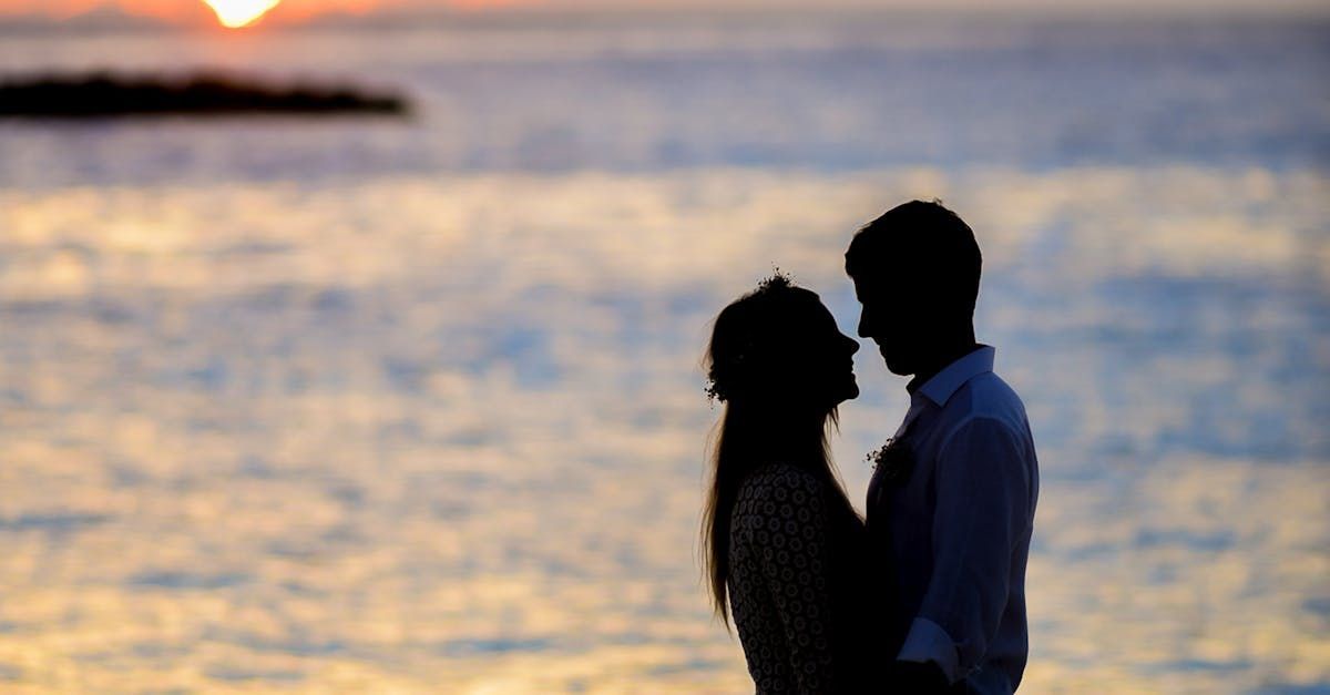 A man and a woman are kissing on the beach at sunset.