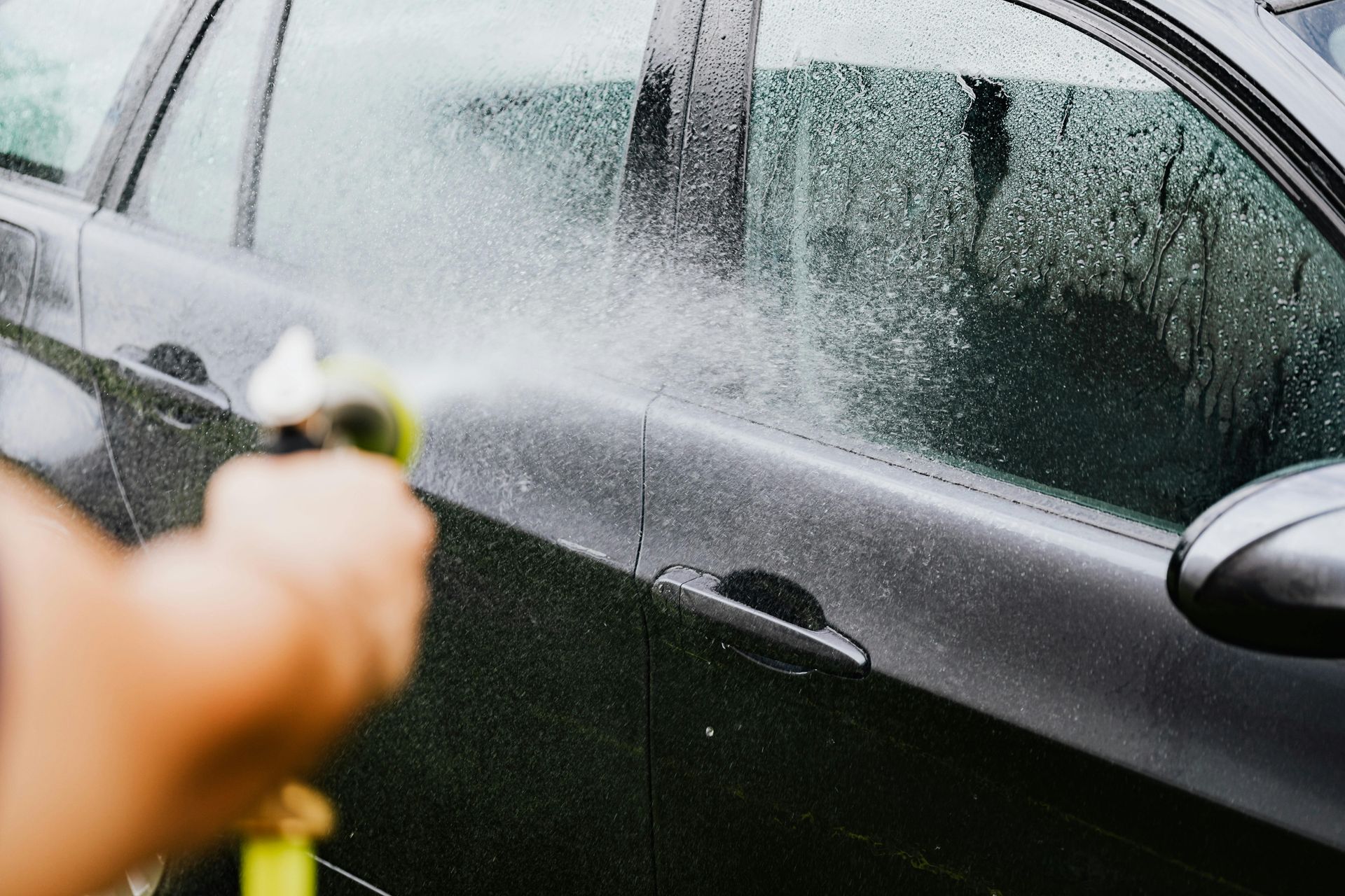 A person is washing a car with a hose.