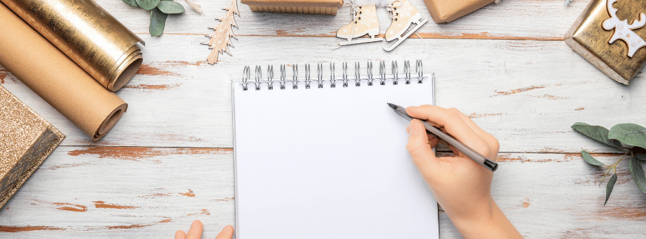 A person is writing in a notebook on a wooden table.