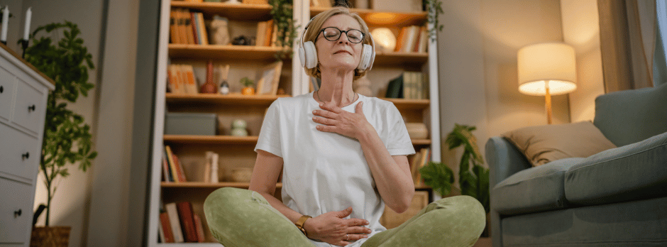 A woman is sitting on the floor in a living room wearing headphones and meditating.