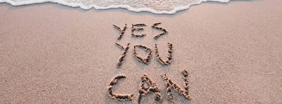 The words yes you can are written in the sand on a beach.