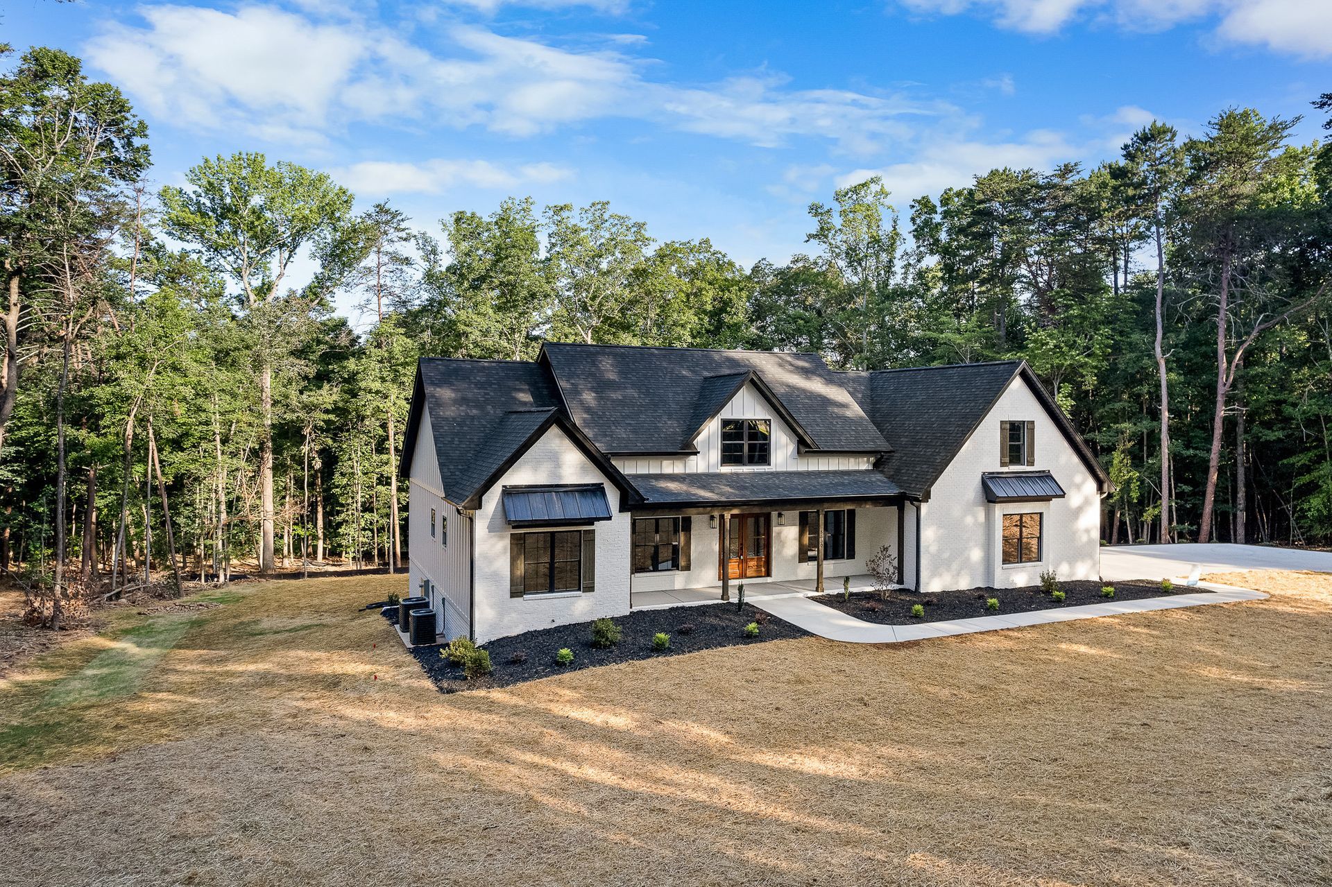 A white house with a black roof is sitting on top of a dirt field surrounded by trees.