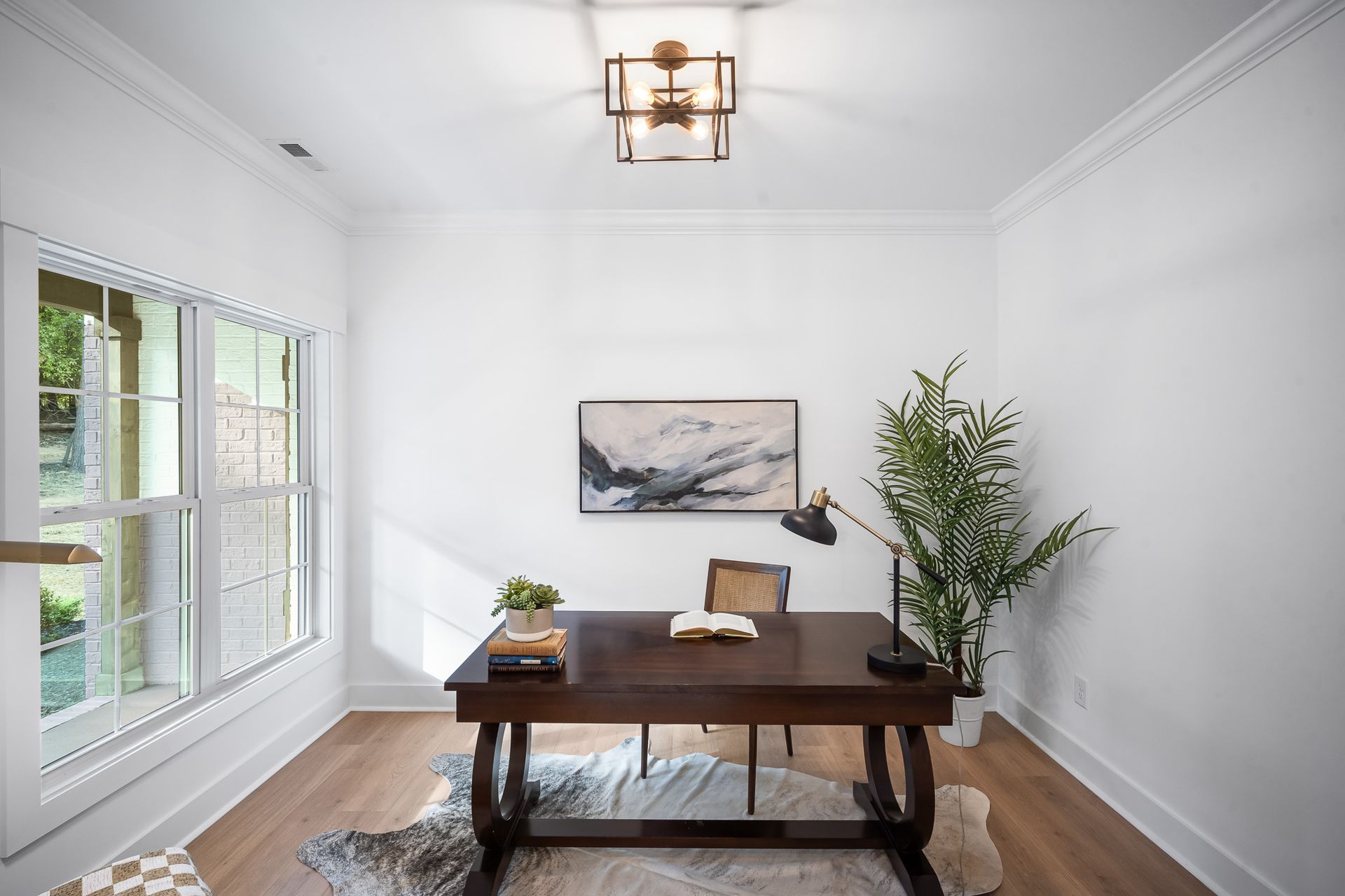 A home office with a desk , chair , lamp and painting on the wall.