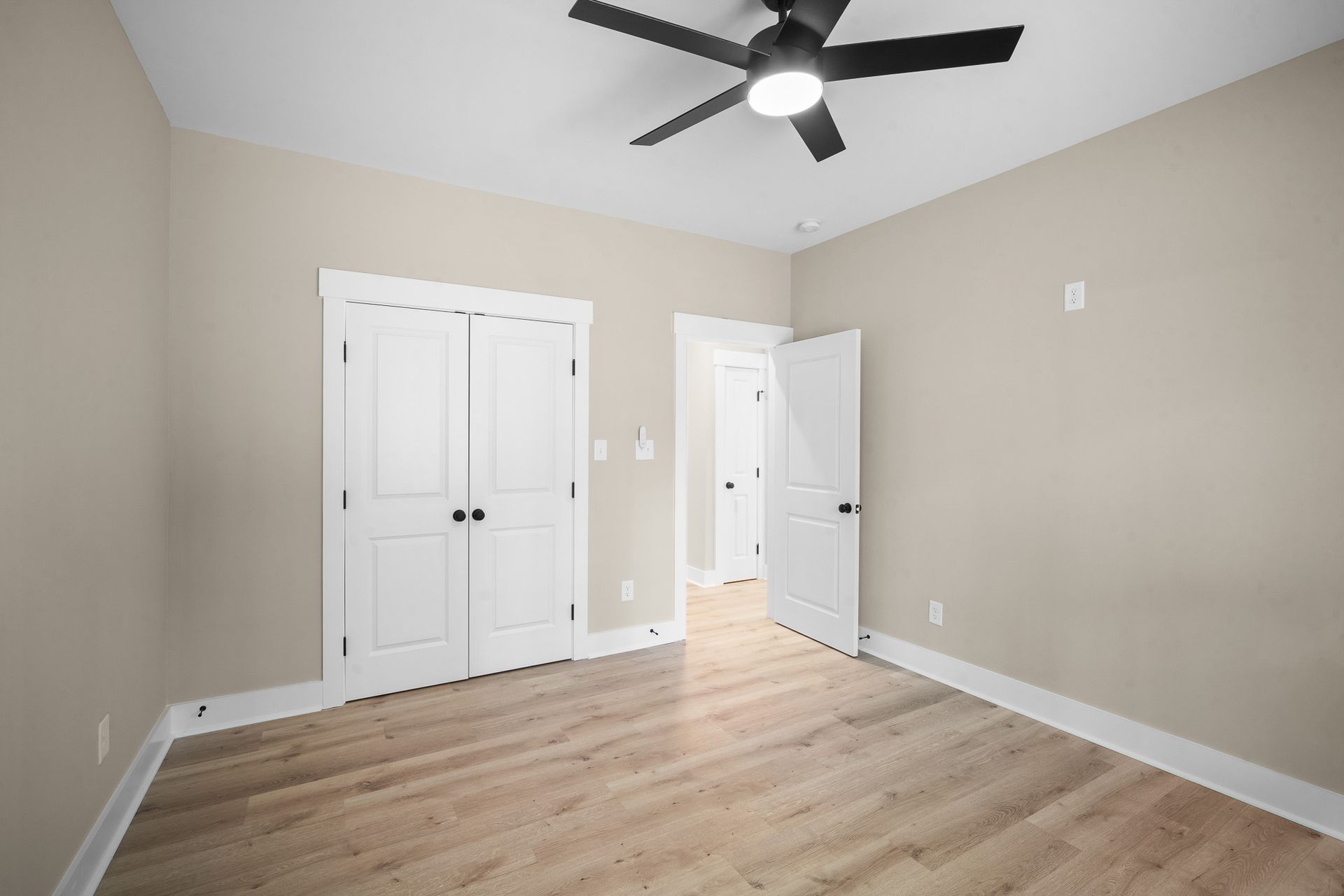 An empty bedroom with hardwood floors and a ceiling fan.