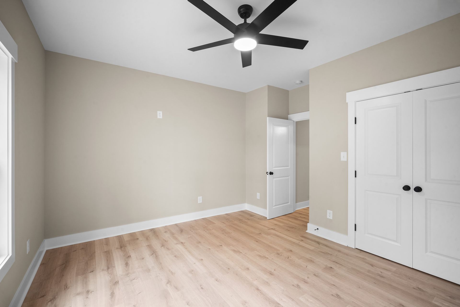 An empty bedroom with hardwood floors and a ceiling fan.