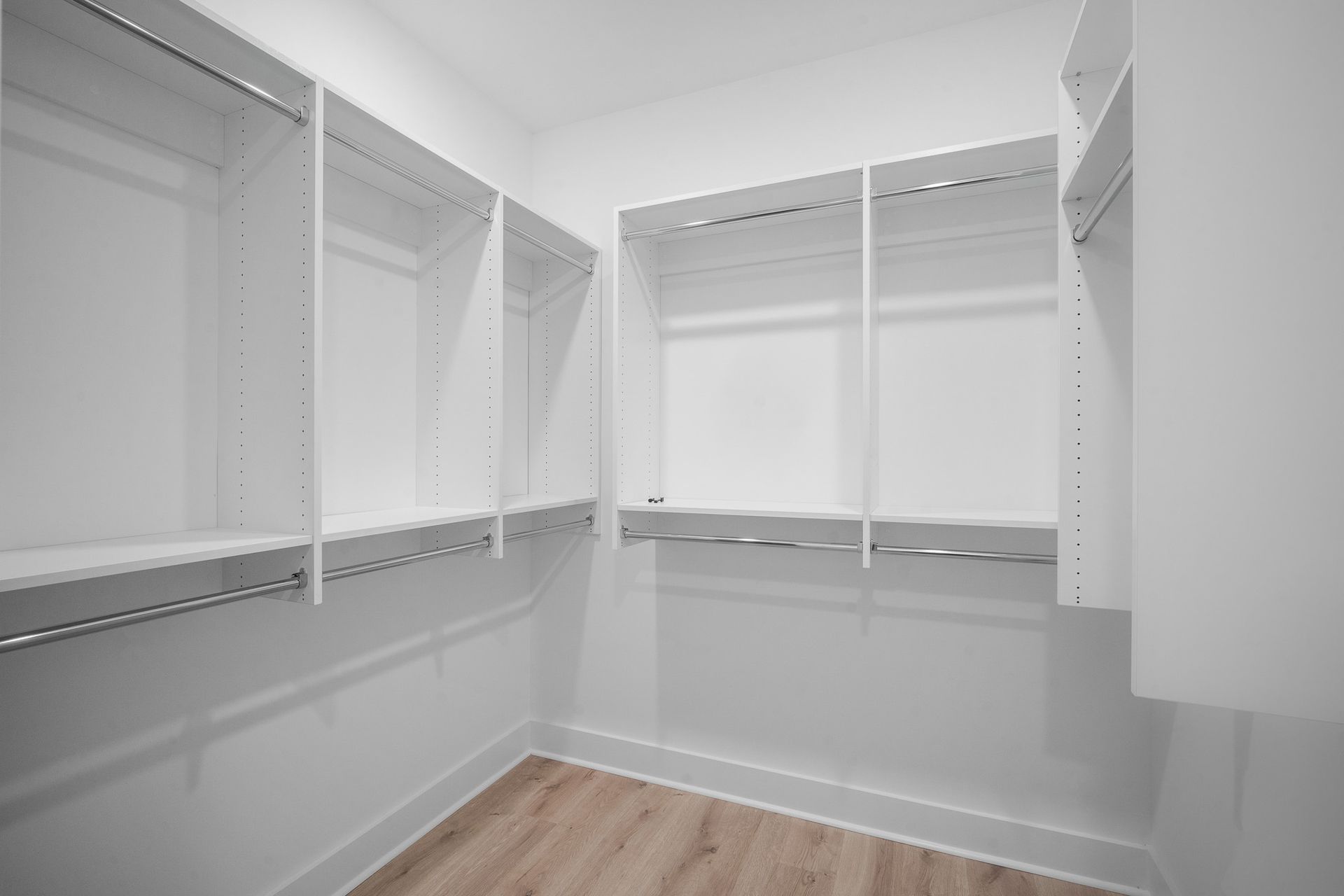 An empty walk in closet with white shelves and wooden floors.