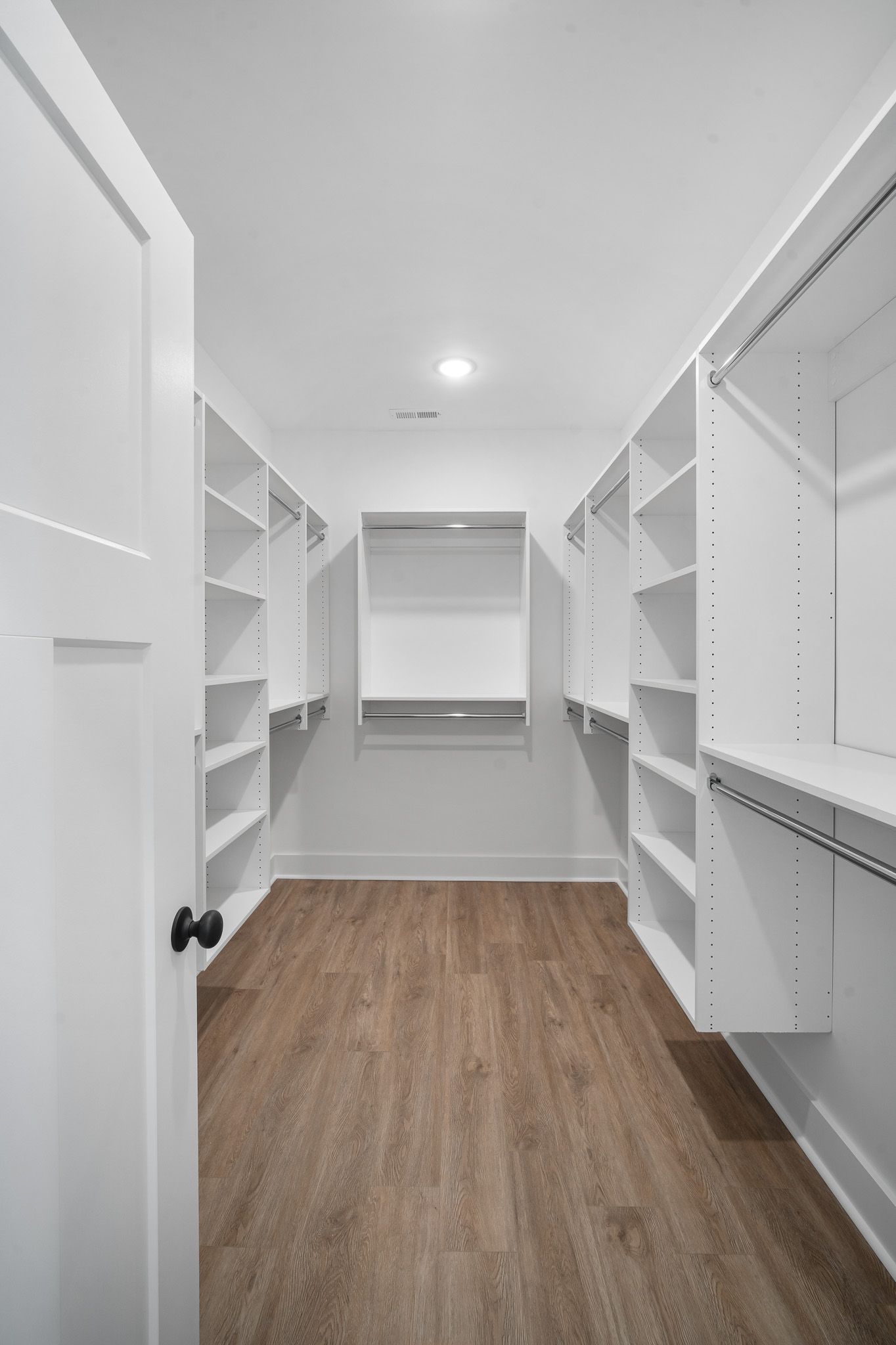 A walk in closet with wooden floors and white shelves.