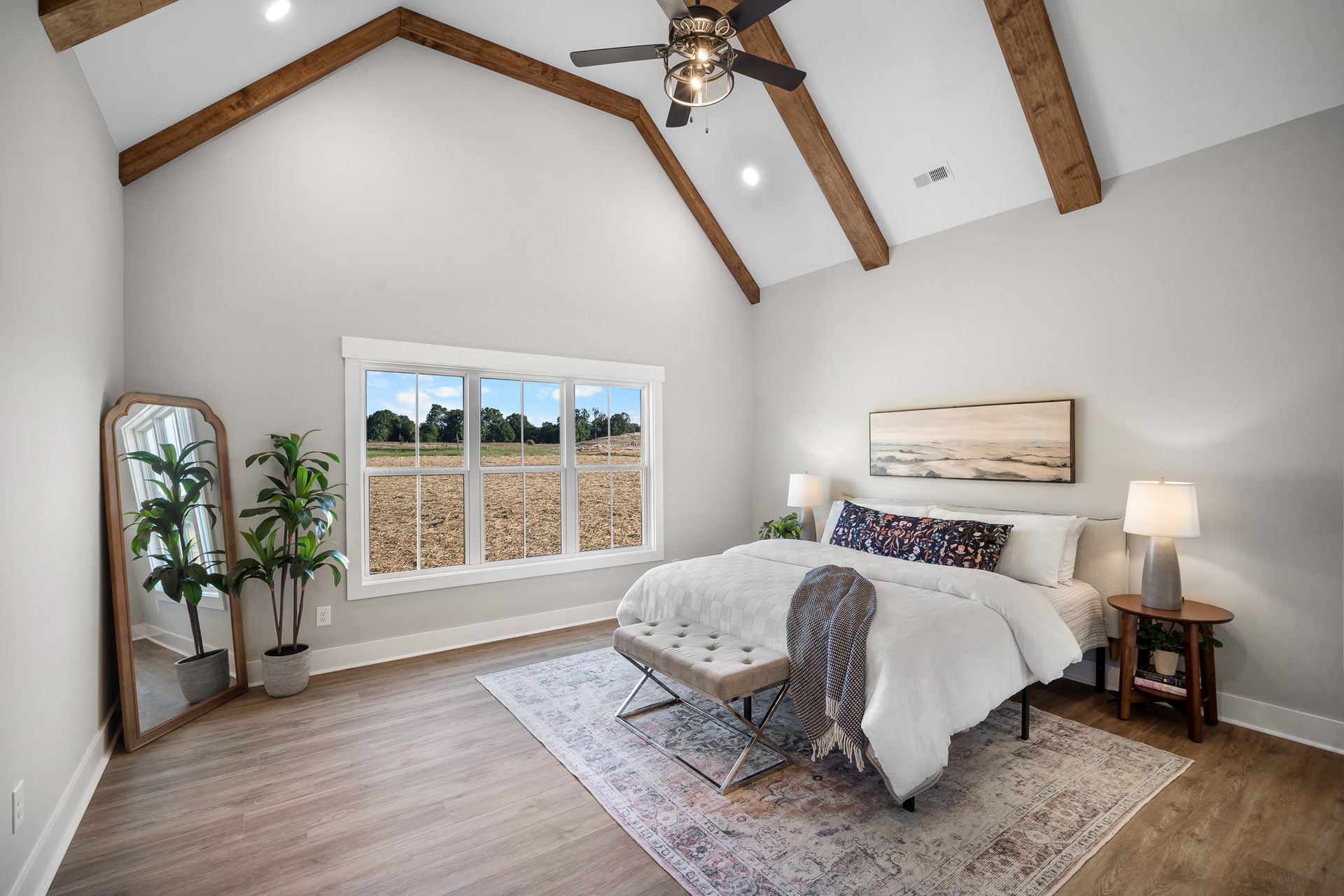 A bedroom with a bed , mirror , bench and ceiling fan.