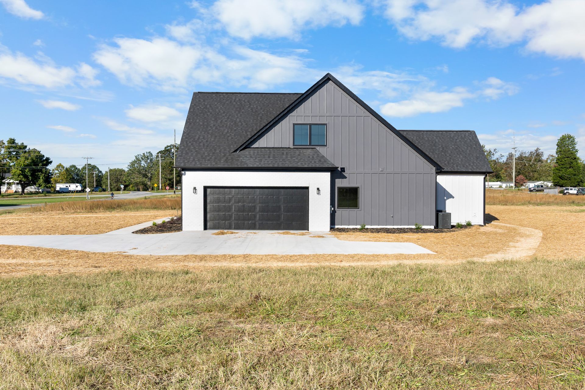 A house with a garage is sitting in the middle of a grassy field.