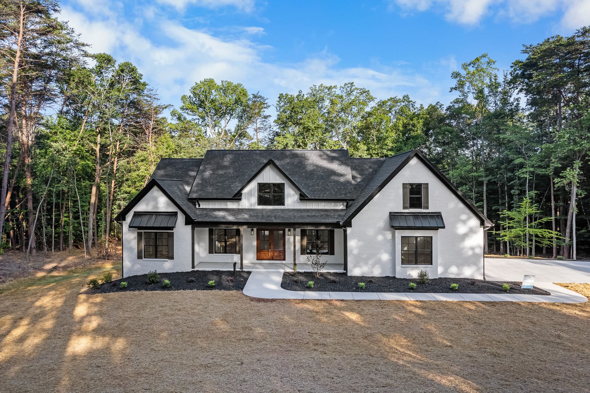 A white house with a black roof is sitting in the middle of a forest.