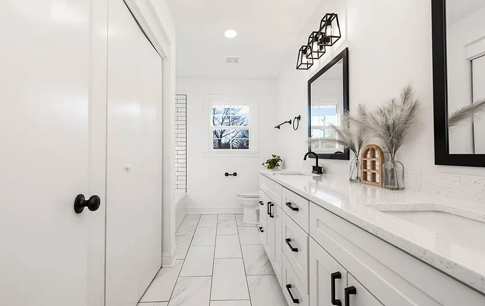 A bathroom with white cabinets , a sink , a mirror and a toilet.