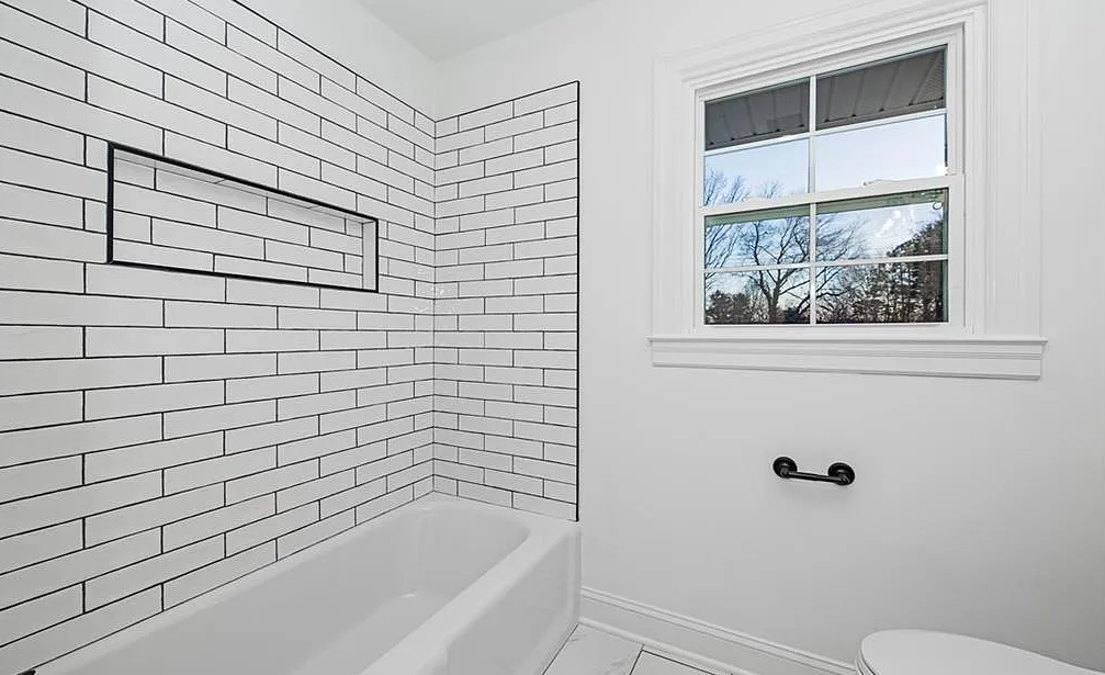 A bathroom with white brick walls , a tub , a toilet and a window.
