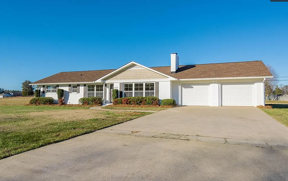 A white house with a brown roof and a driveway in front of it.