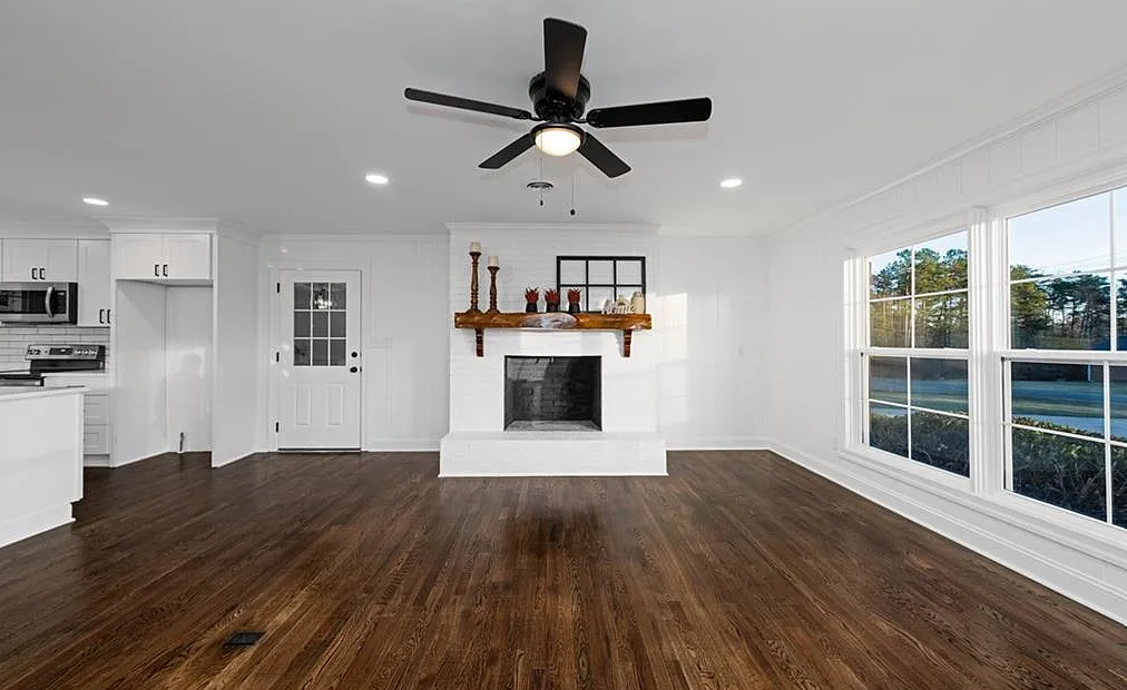 An empty living room with hardwood floors , a fireplace and a ceiling fan.