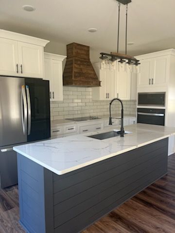 A kitchen with white cabinets , a stainless steel refrigerator , a sink , and a large island.