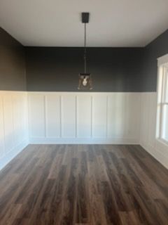 An empty room with wooden floors and a light fixture hanging from the ceiling.