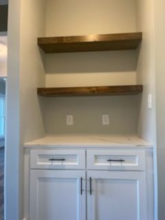 A kitchen with white cabinets and wooden shelves.