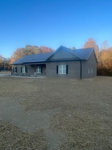 A brick house is sitting in the middle of a dry grass field.