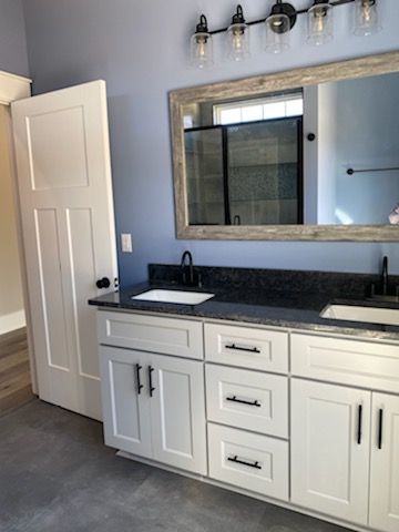 A bathroom with white cabinets , a sink , and a large mirror.