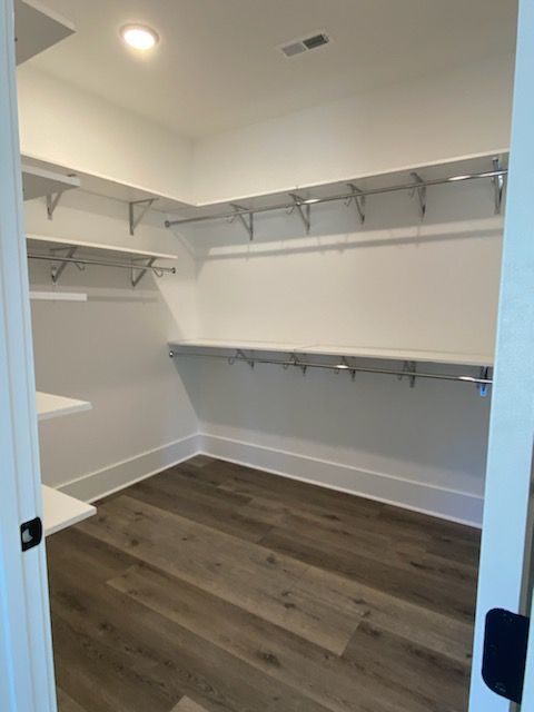 A walk in closet with hardwood floors and white shelves.