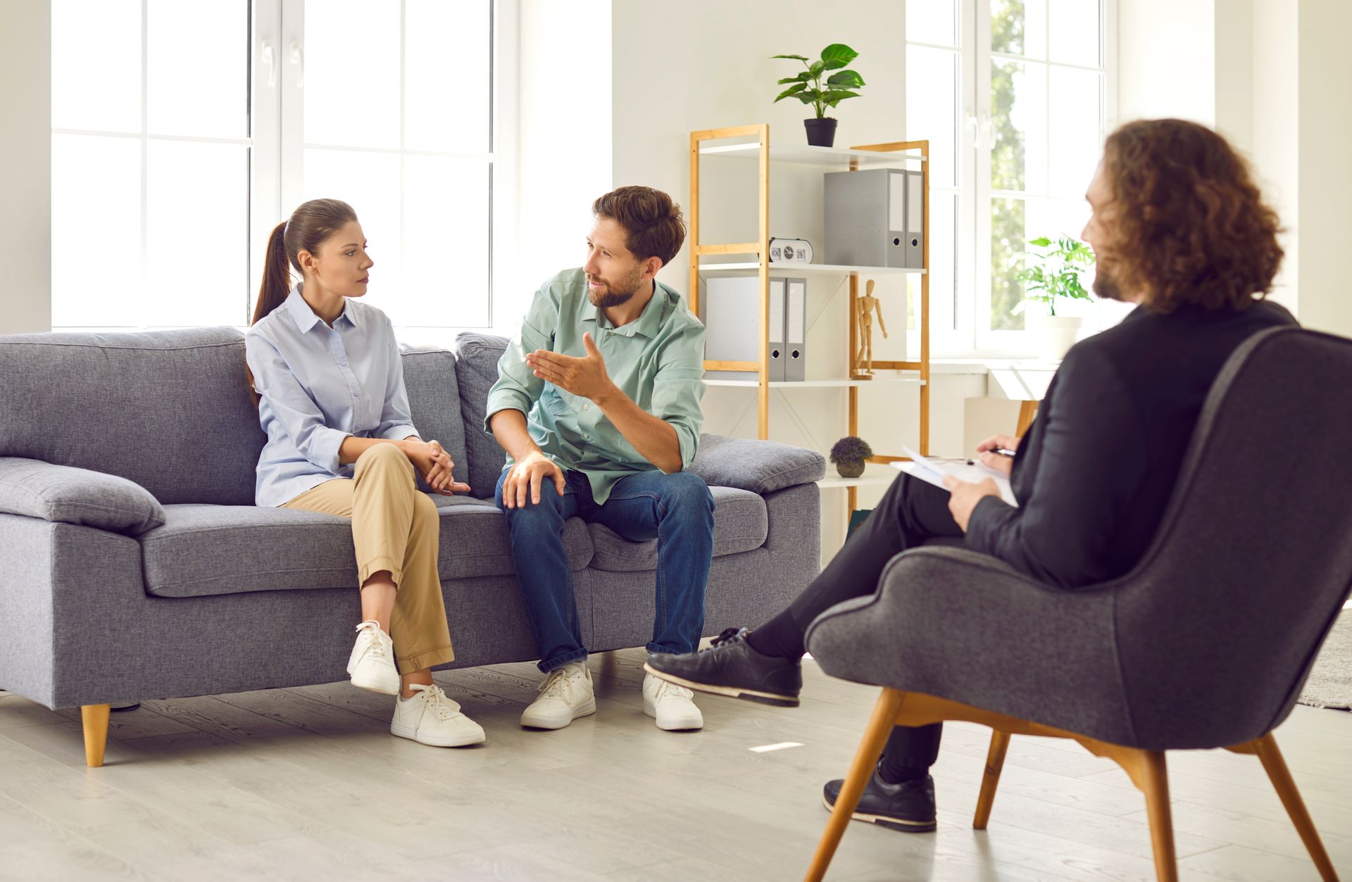 Couple talking with a therapist in a light-filled office; the therapist is taking notes.