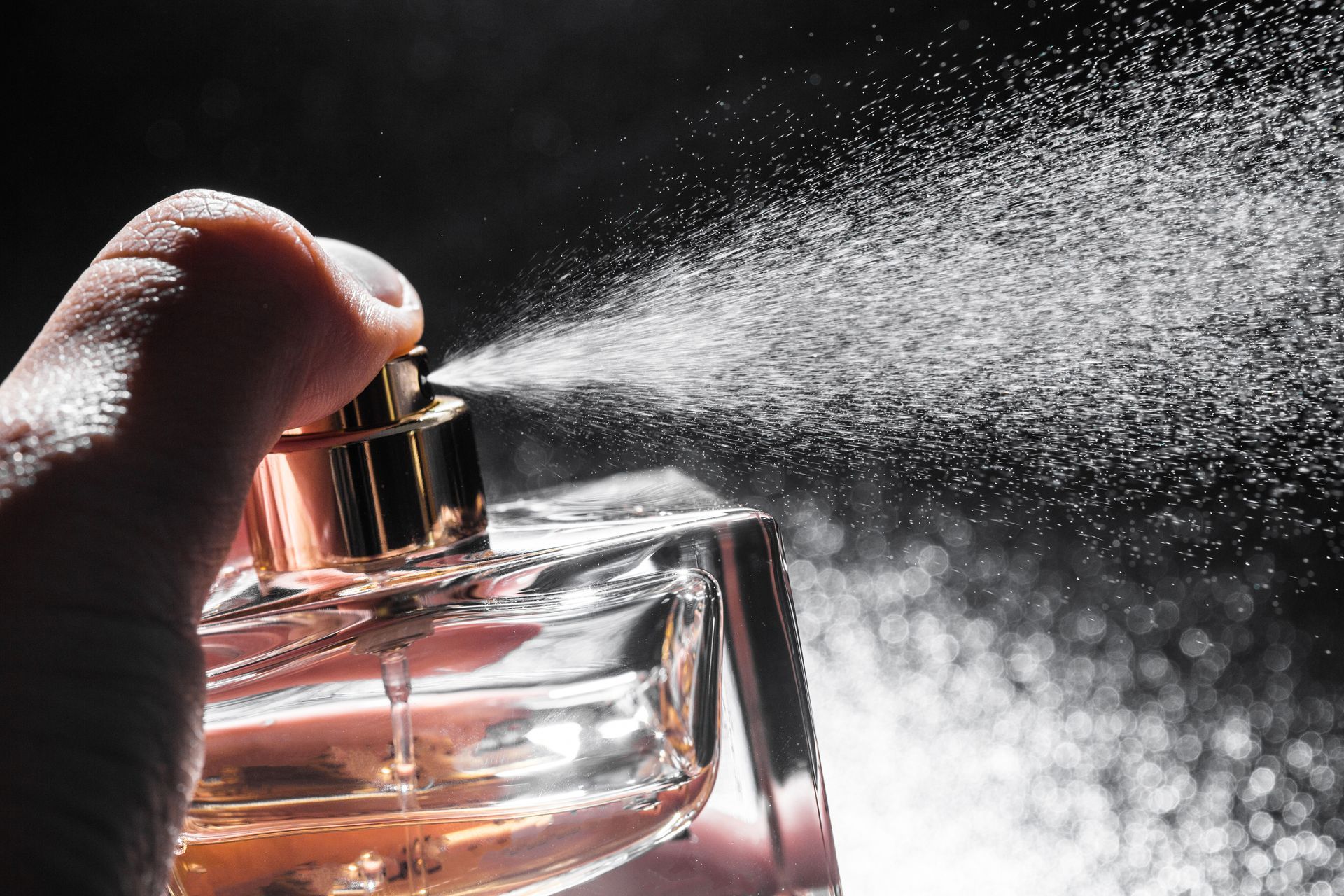 Hand spraying perfume bottle, creating a cloud of mist against a dark background.