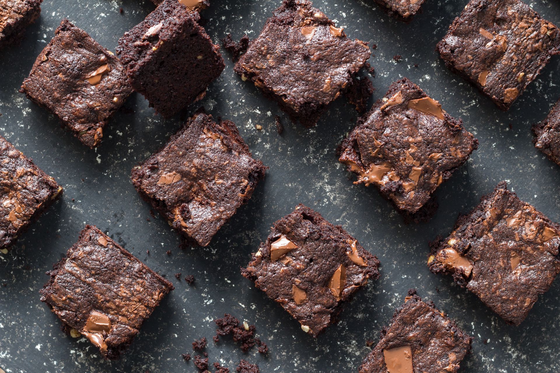 Brownies, square-cut on a dark surface, with visible chocolate chunks.