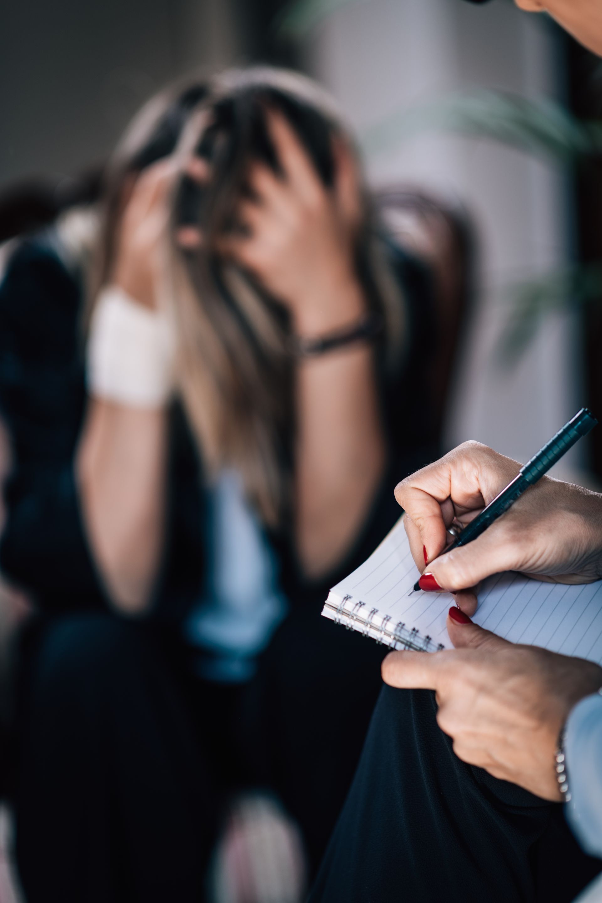 Therapist taking notes during a session with a distressed person holding their head.