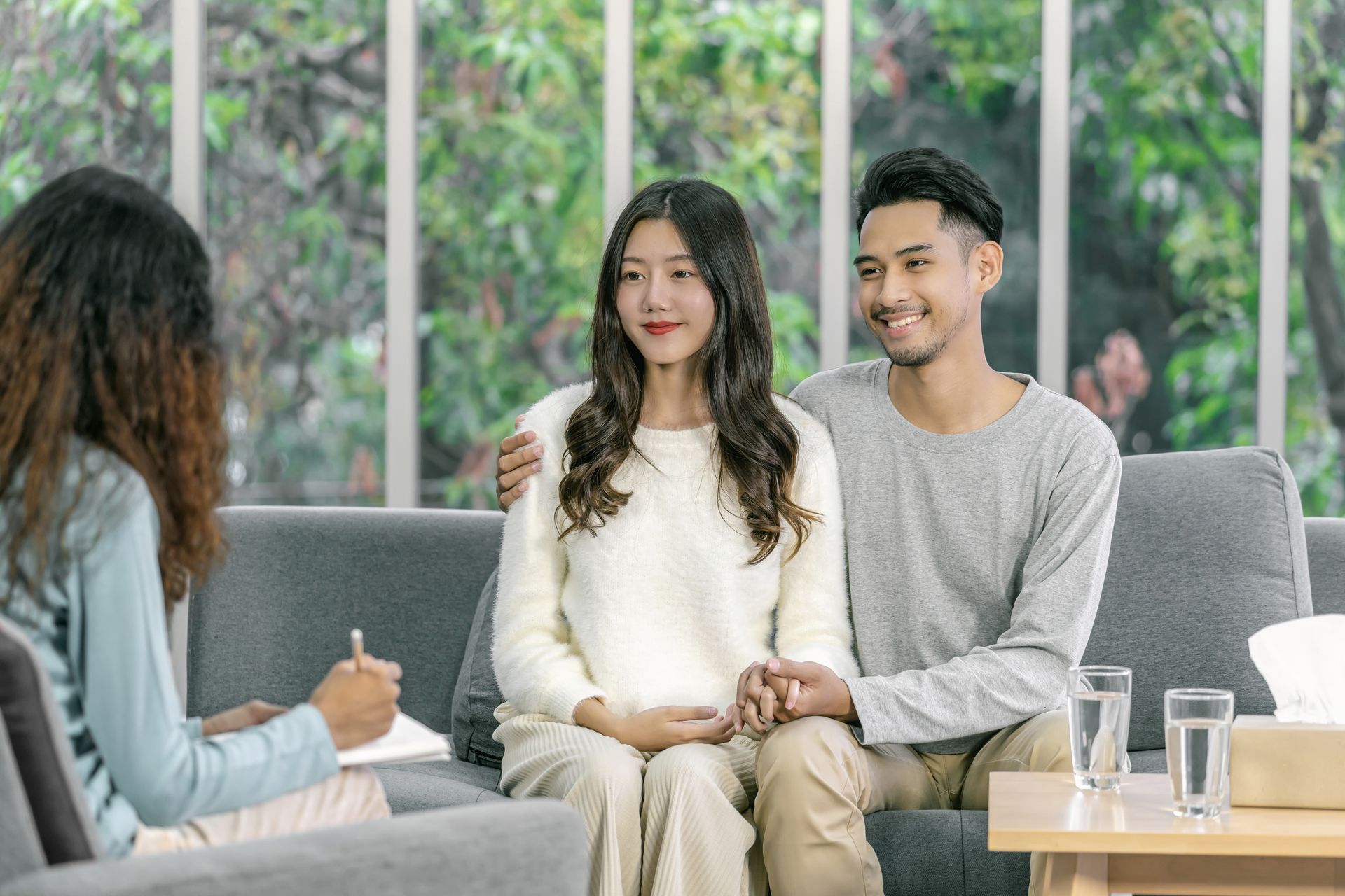 Couple in counseling session, sitting together on a couch, holding hands, talking to a therapist.