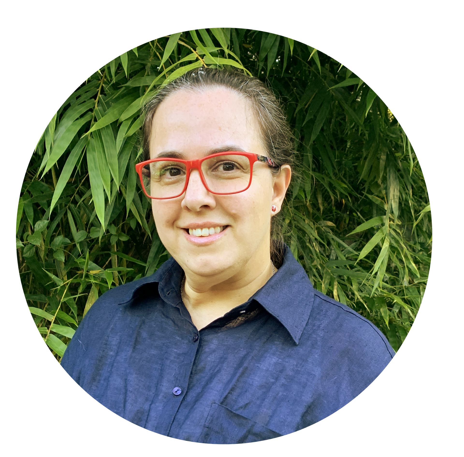 Mujer con gafas rojas sonríe, vistiendo camisa azul, frente al bambú.