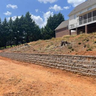 A large house is sitting on top of a hill next to a stone wall.
