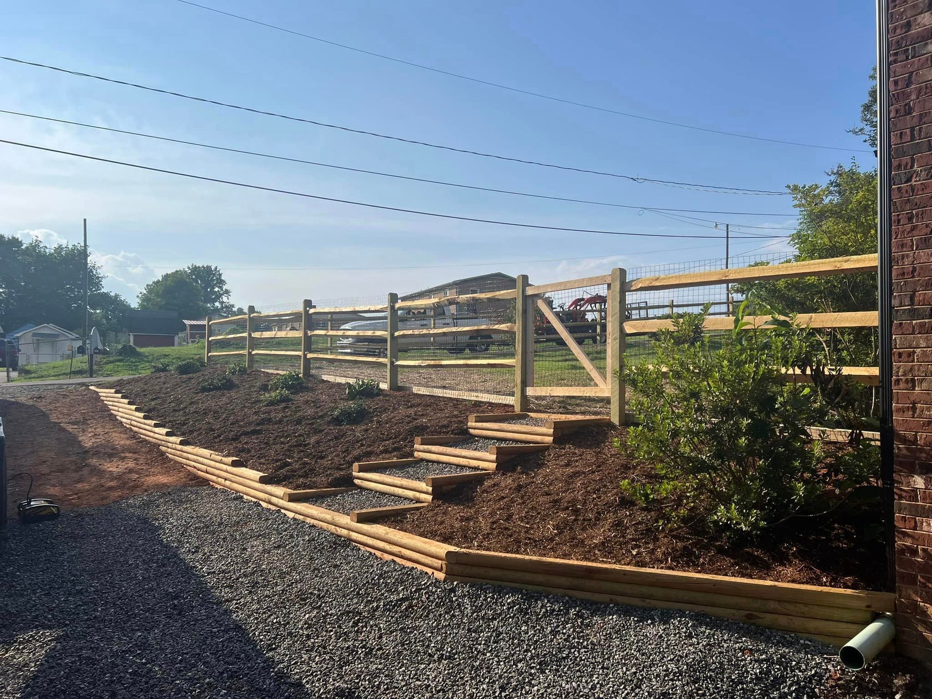 A wooden fence surrounds a gravel driveway next to a brick building.