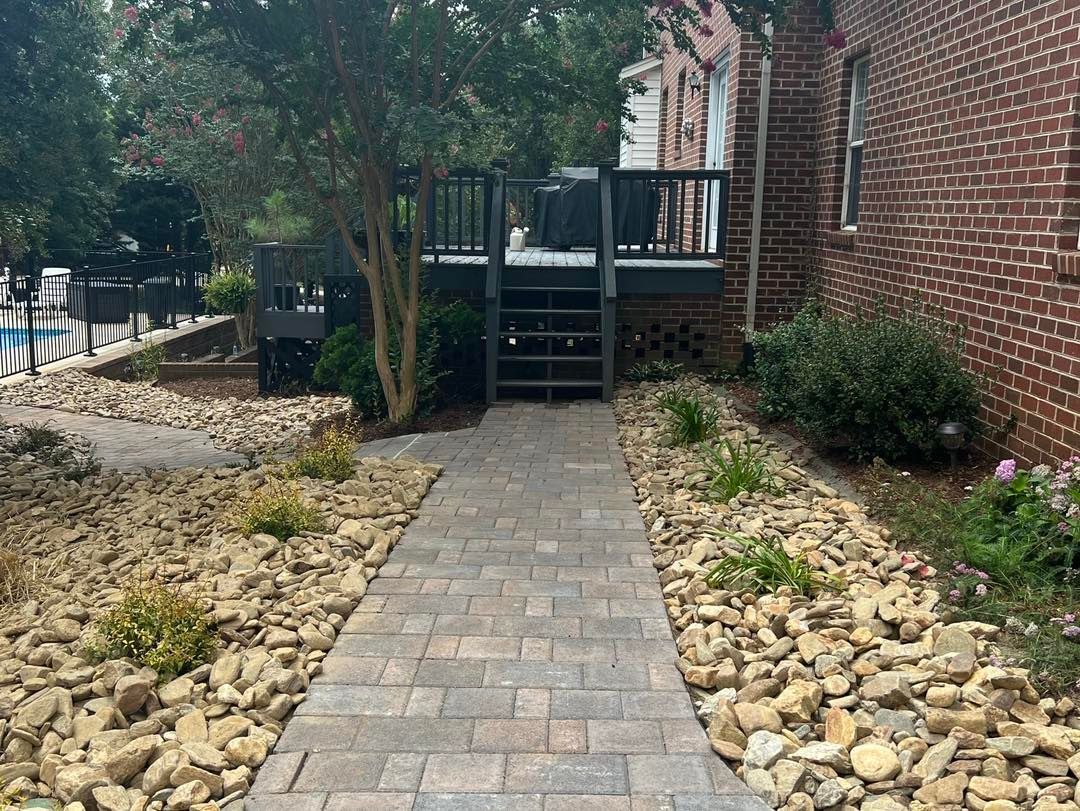 A brick walkway leading to a house with a deck and stairs.