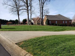 A house is sitting on top of a lush green field next to a road.